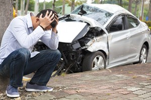 man near wrecked car with head in hands