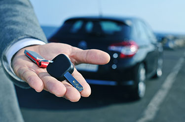 closeup of person holding keys in front of a car